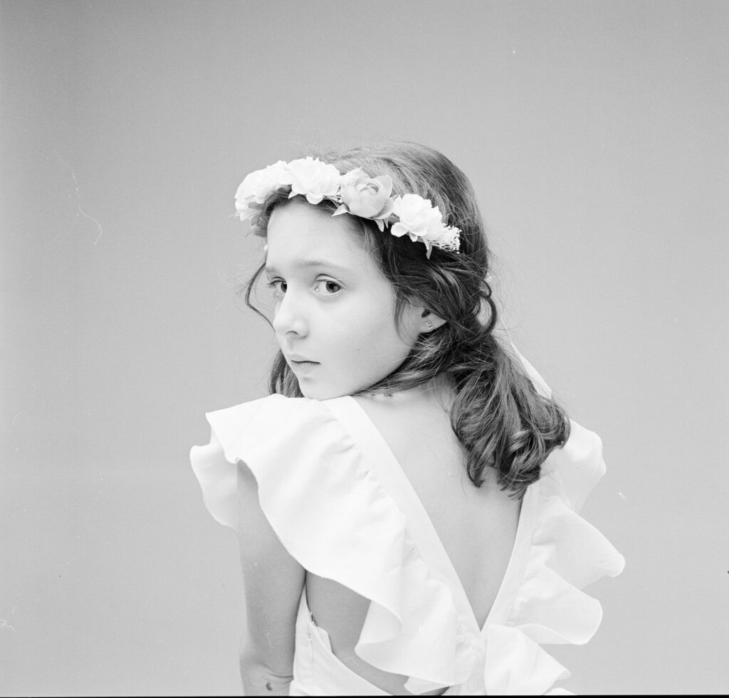 Session en studio avec Emmy, une jeune fille en élégante robe de ceromonie blanche et sa couronne de fleurs coordonnées.